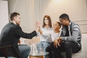 Family joyfully high-fiving while sitting on a sofa indoors, promoting teamwork and unity.